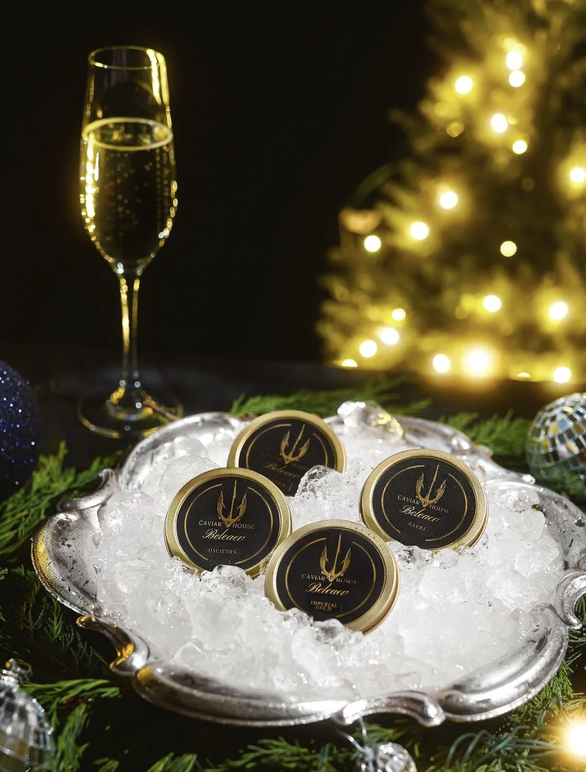 Caviar tins on ice beside champagne and Christmas lights