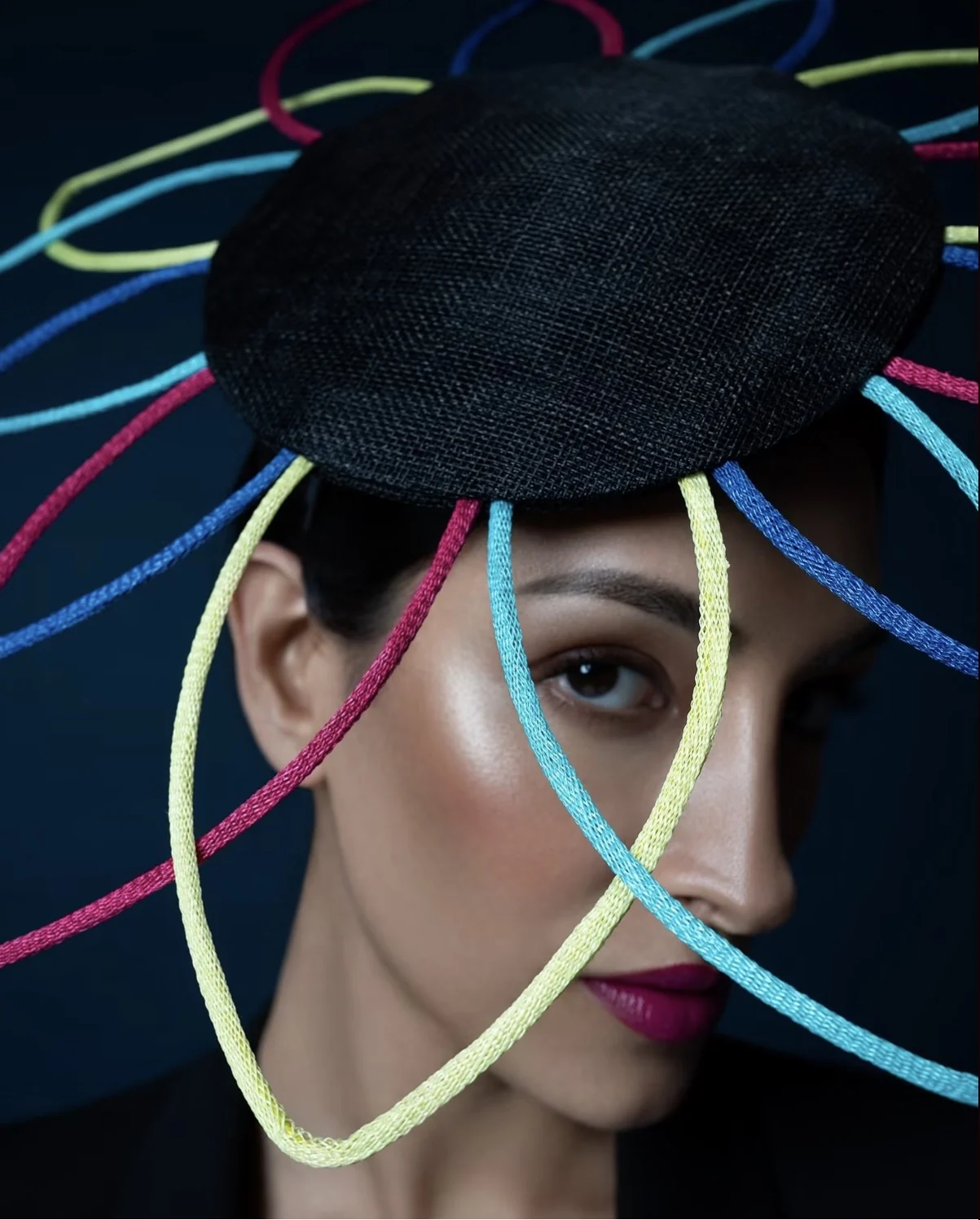 Close-up portrait framed by a multicolour sculptural hat